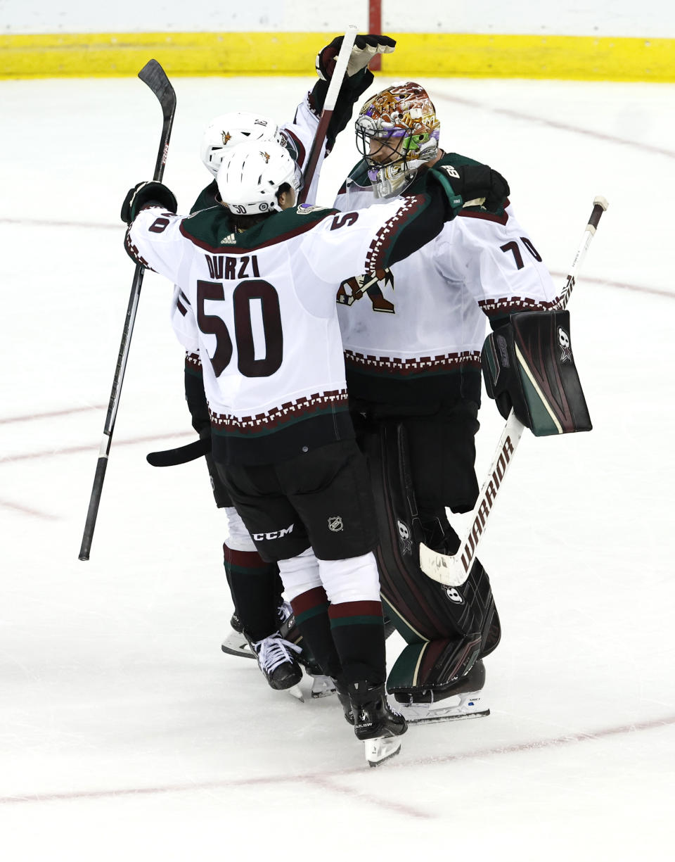 Arizona Coyotes defenseman Sean Durzi (50) celebrates with goaltender Karel Vejmelka (70) after defeating the New Jersey Devils in a shootout of an NHL hockey game Friday, Oct. 13, 2023, in Newark, N.J. (AP Photo/Noah K. Murray)