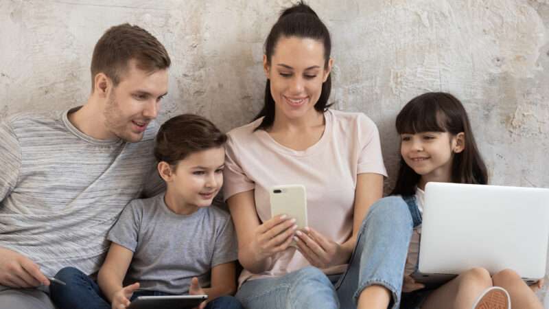 A family gathers around a cell phone and a laptop
