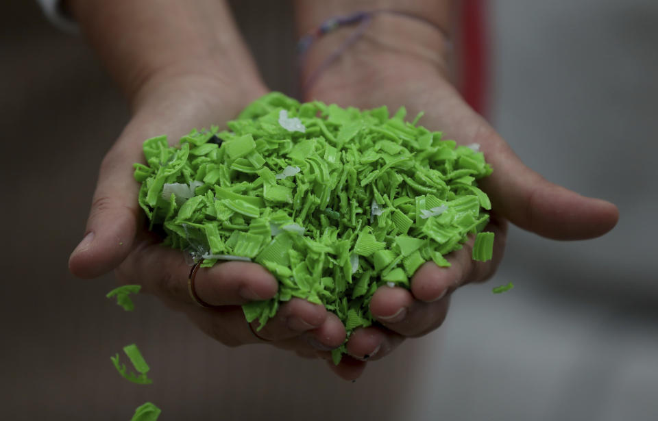 A worker shows shredded bottle caps that will be transformed into raw material to make different plastic articles at the Colorplastic company in Bogota, Colombia, Friday, April 9, 2021. Sajú is a company that makes sunglasses from old plastic lids, like those on soda bottles. The company buys bottle tops that have been turned into small pellets by a recycling plant, melts down the material and injects it into molds to produce colorful frames. Dark lenses are then mounted on the frames, to make shades that are sold at Sajú's stores for about $40 each. (AP Photo/Fernando Vergara)