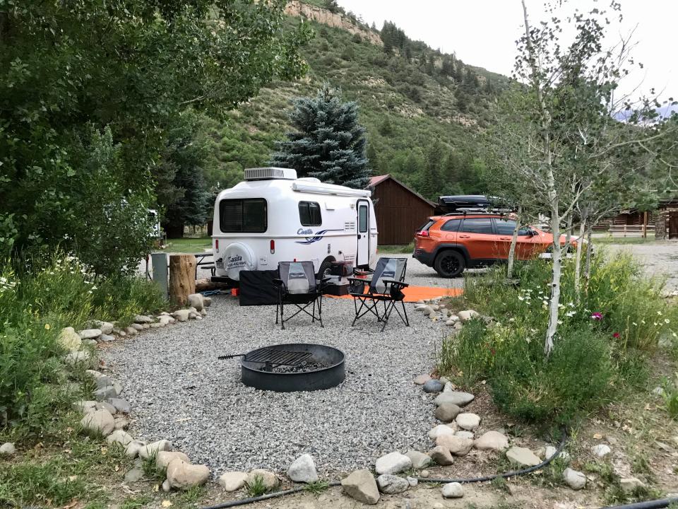 A campsite with a trailer and car surrounded by trees