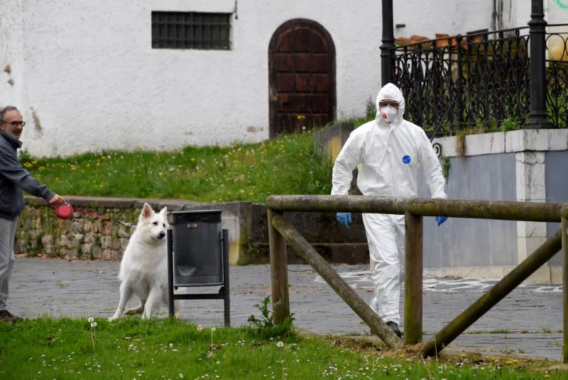 A sanitary worker walks past a man with a dog near the nursing home where a woman died and several residents and care providers have been diagnosed with coronavirus disease (COVID-19) in Grado