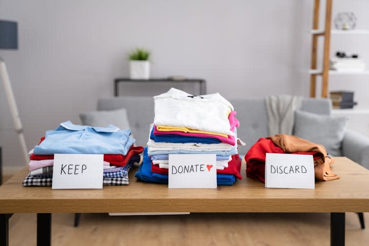 Three piles of neatly folded clothes with paper signs reading keep, donate and discard