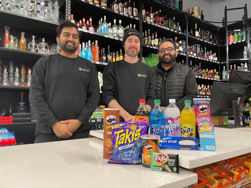 From left, Quest Spirits co-owner Kish Sutariya, general manager Adam Starnes, and co-owner Chin Pathak grab some of their favorite harder-to-find snack food flavors at the new Whitmore Lake convenience store, Tuesday, Jan. 18, 2022.