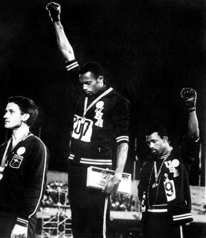 US sprinters Tommie Smith (C) and John Carlos (R) raise their gloved fists in the Black Power salute to express their opposition to racism in the USA during the medal ceremony (-)