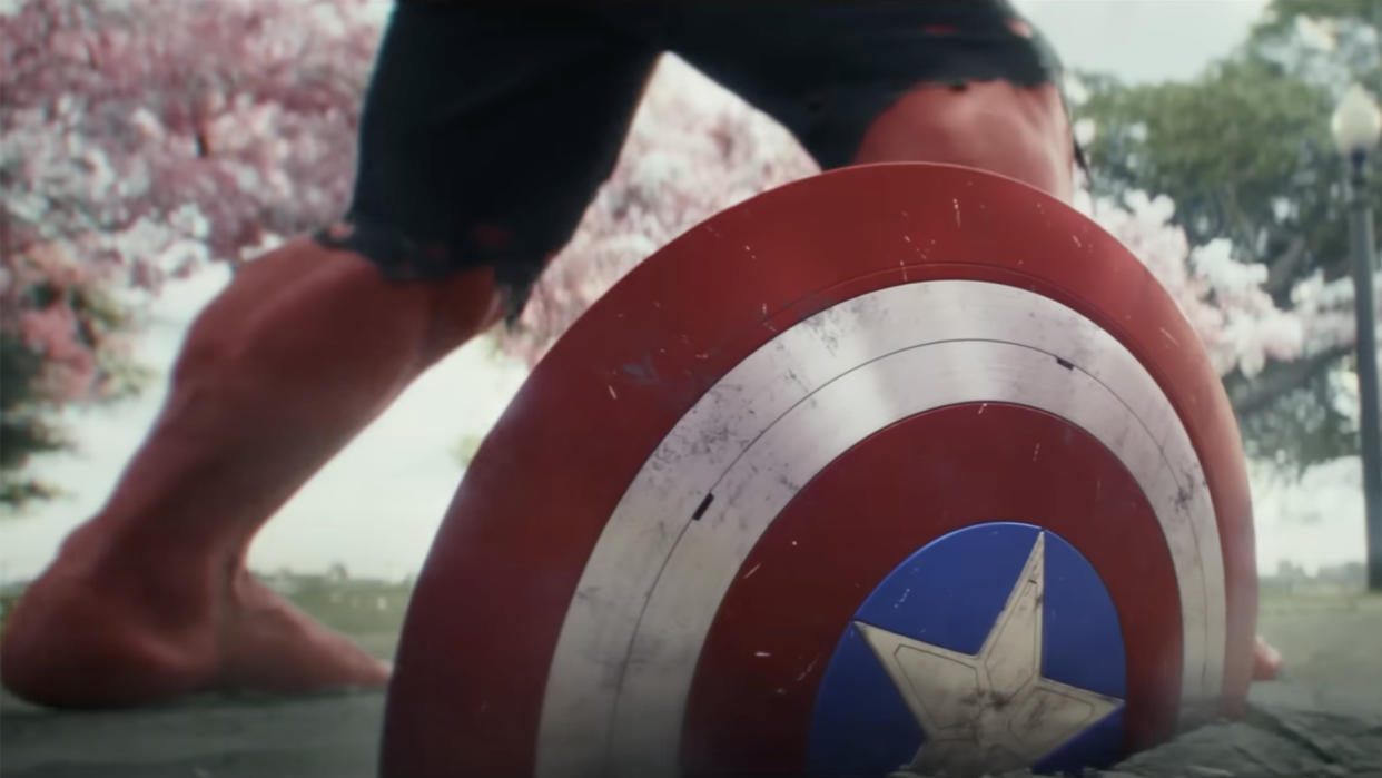  The legs of red hulk appear behind captain america's shield . 