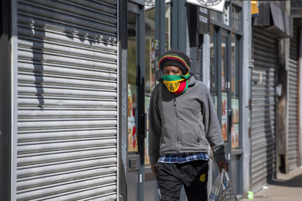 A man uses a scarf as a face mask as he walks past closed shops in Leeds city centre, West Yorkshire on April 14, 2020, as life in Britain continues during the nationwide lockdown to combat the novel coronavirus COVID-19 pandemic. - Britain's economy could shrink by an unprecedented 13 percent this year in the case of a three-month coronavirus lockdown, according to a scenario published Tuesday by fiscal watchdog the Office for Budget Responsibility. (Photo by Anthony Devlin / AFP) (Photo by ANTHONY DEVLIN/AFP via Getty Images)