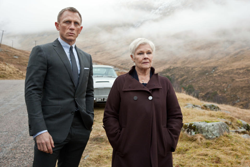 Daniel Craig and Judi Dench stand by the side of a road