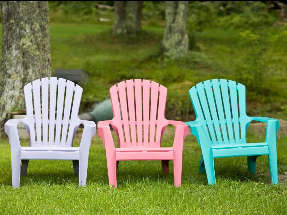 Three plastic lawn chairs on lawn. The chairs are light-gray, pink, and teal