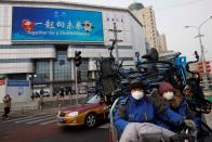 People transport sharing bikes past a billboard advertising the Beijing 2022 Winter Olympics as the coronavirus disease (COVID-19) continues in Beijing