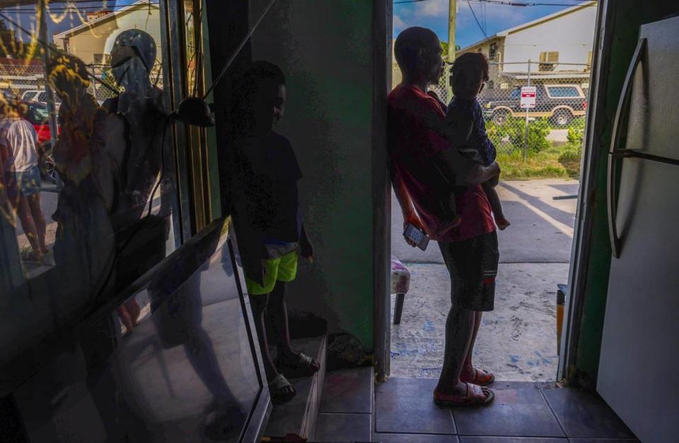 Mario Sauveur, 32, holding his son, talks with neighbors through the open door of his trailer.