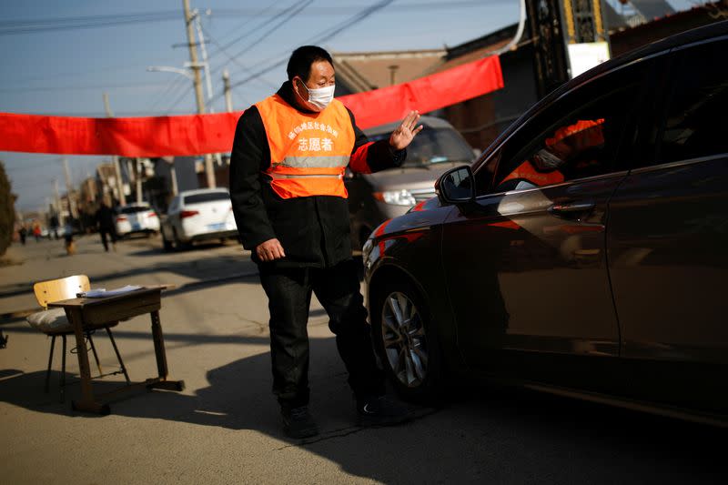 A village committee member wearing face mask and vest, stops a car for checking as he guards at the entrance of a community to prevent outsiders from entering, as the country is hit by an outbreak of the new coronavirus, in Tianjiaying village, outskirts o