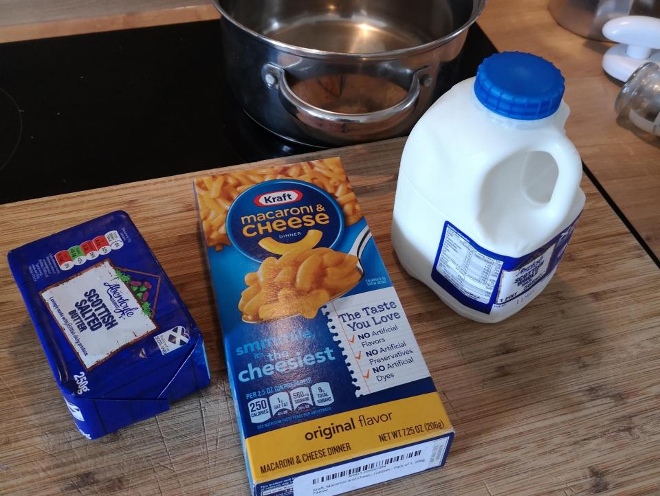 A pot, butter, kraft mac and cheese, and milk on a wooden counter
