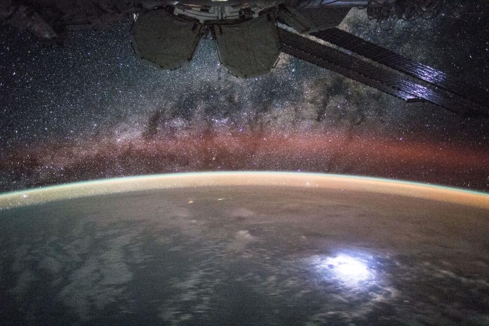 earth with bright spot lightning strike with starry milky way purple and black above and solar panels of space station in foreground