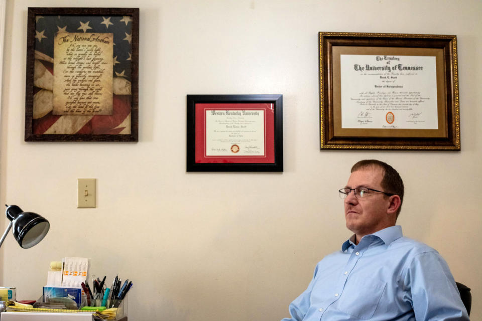 Image: Derek Scott sits at a desk with framed degrees on the wall above him. (Hannah Rappleye / NBC News)