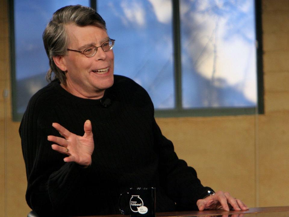 stephen king waiving while sitting at a table