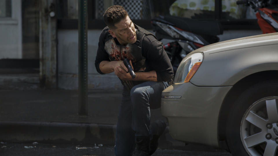 Jon Bernthal holding gun and hiding behind car as The Punisher