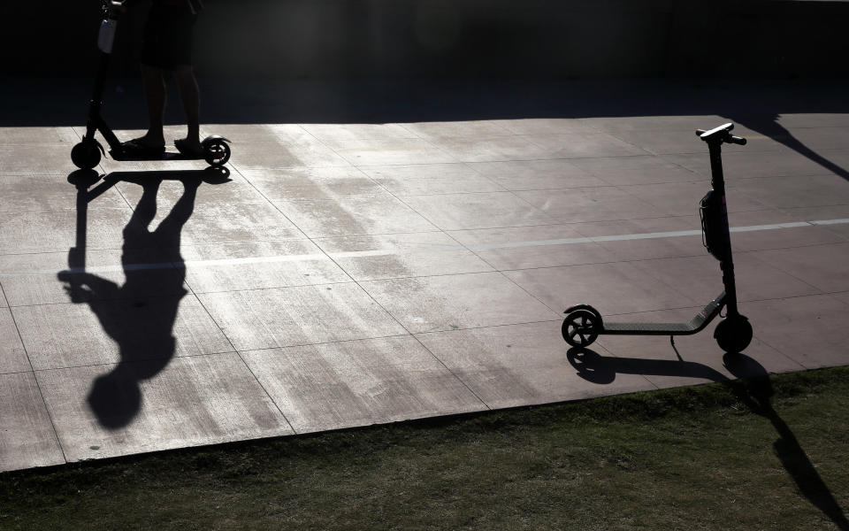 FILE - In this May 28, 2019, file photo a man on a scooter passes a parked scooter along the Mission Beach boardwalk in San Diego. San Diego is suing scooter companies to get them to pay the city's costs to defend any lawsuits generated by the two-wheeled vehicles that have proliferated on public sidewalks. (AP Photo/Gregory Bull, File)