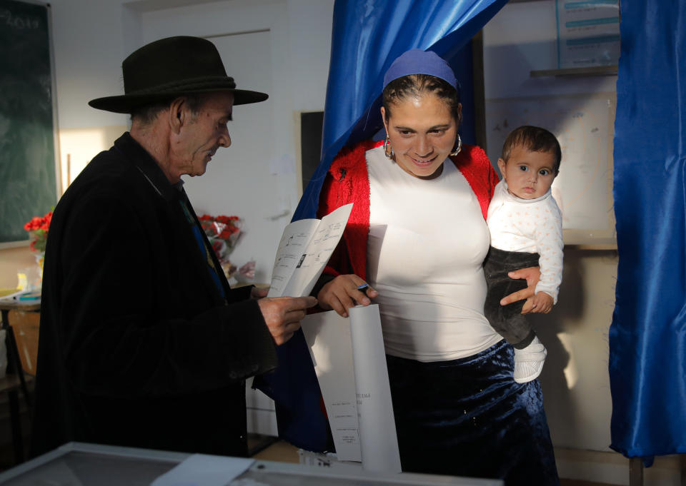 Baby Sonia is held by her mother as she casts her vote at a polling station in Sintesti, Romania, Sunday, Nov. 10, 2019. Romania held a presidential election Sunday after a lackluster campaign that has been overshadowed by the country's political crisis, which saw a minority government installed just a few days ago. (AP Photo/Vadim Ghirda)