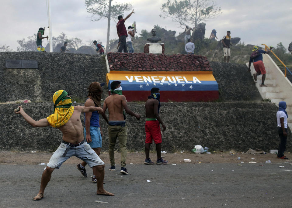 Manifestantes venezolanos lanzan piedras durante enfrentamientos con las autoridades en la frontera entre Venezuela y Brasil, el sábado 23 de febrero de 2019. Miles de personas permanecen en Pacaraima, en el cruce fronterizo internacional de la ciudad con Venezuela para exigir el ingreso de alimentos y medicinas. (AP Foto/Ivan Valencia)