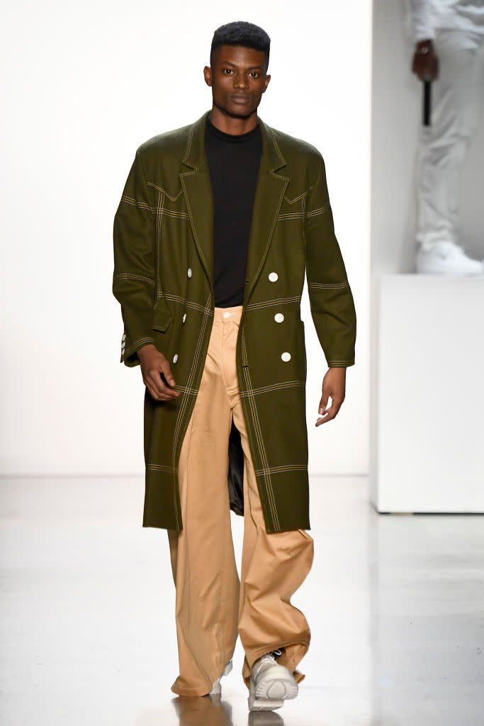 <p>Model wears a hunter green coat, black top, and tan trousers at the Pyer Moss FW18 show. (Photo: Getty) </p>