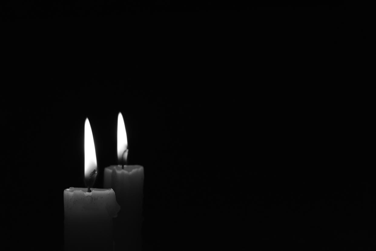 Light candle burning brightly in the black background. Candle flame. Black and white photo. There's room for your text. The concept of mourning, grief or sorrow.