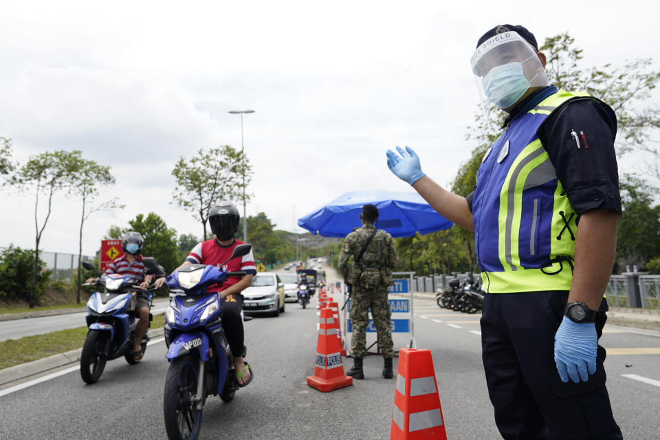 Police officers check vehicles at a roadblock to ensure that people abide by a movement control order on the outskirts of Kuala Lumpur, Malaysia, Wednesday, Oct. 14, 2020. Malaysia will restrict movements in its biggest city Kuala Lumpur, neighboring Selangor state and the administrative capital of Putrajaya from Wednesday to curb a sharp rise in coronavirus cases. (AP Photo/Vincent Thian)