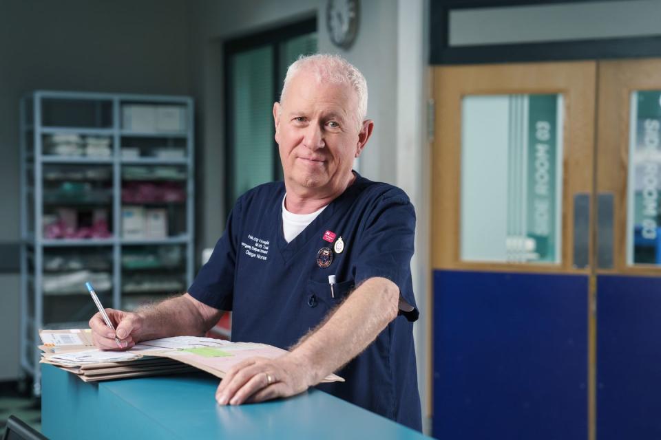 casualty star derek thompson in character as charlie fairhead, writing in a medical report at the nurses' station