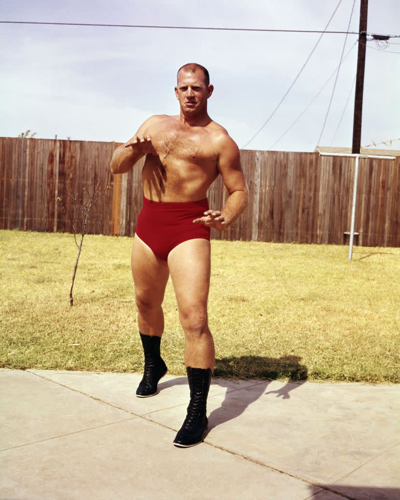 fritz von erich standing in a yard with a fence pretending to square up to an opponent in his wrestling attire