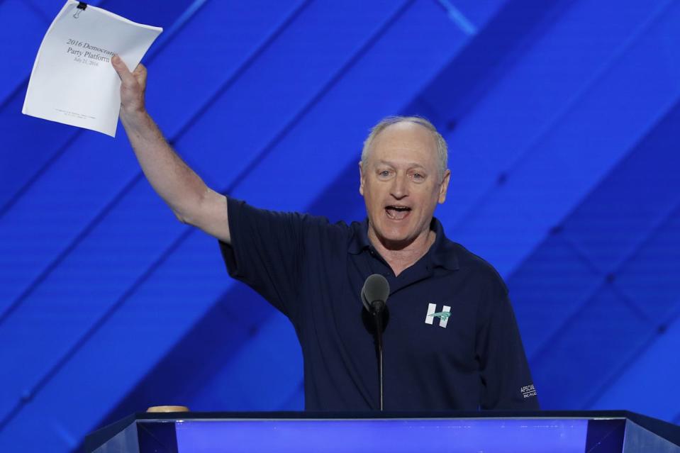 A man at a lectern holds up a group of papers.