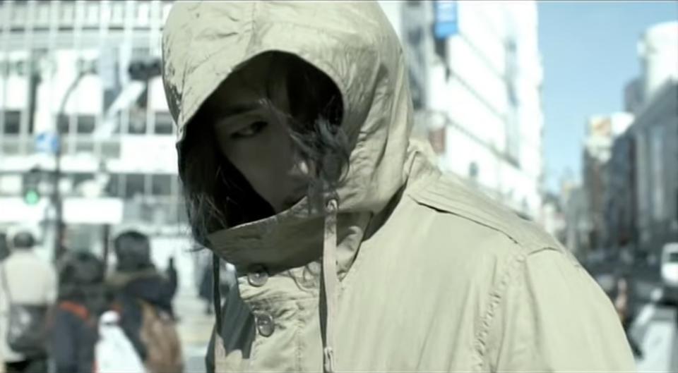 Screenshot from "I am Ichihashi: Journal of a Murderer," with actor Dean Fujioka playing Ichihashi; he's walking in a crowded street hiding his face under a brown hoodie