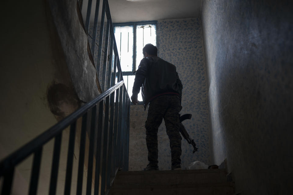 A U.S.-backed Syrian Democratic Forces (SDF) fighter looks out the window from a building recently taken by SDF as the fight against Islamic State militants continues in the village of Baghouz, Syria, Sunday, Feb. 17, 2019. Islamic State militants are preventing more than 1,000 civilians from leaving a tiny area still held by the extremist group in a village in eastern Syria, a spokesman for the U.S.-backed Syrian militia fighting the group said Sunday. (AP Photo/Felipe Dana)