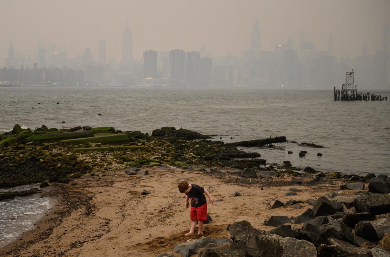 A child stands on the shore before the New York city skyline and east river shrouded in smoke, in Brooklyn on June 5, 2023. Smoke from the hundreds of wildfires blazing in eastern Canada has drifted south. Hundreds of wildfires were burning in Canada on June 6, 2023, according to the Canadian Interagency Forest Fire Centre, as fires have broken out across the country in recent weeks. Quebec alone had more than 150 active blazes across the province, the fire agency said.
