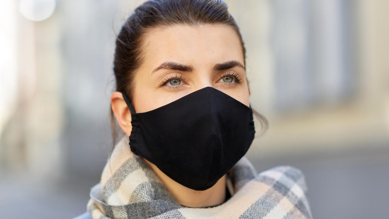 health, safety and pandemic concept - young woman wearing black face protective reusable barrier mask outdoors