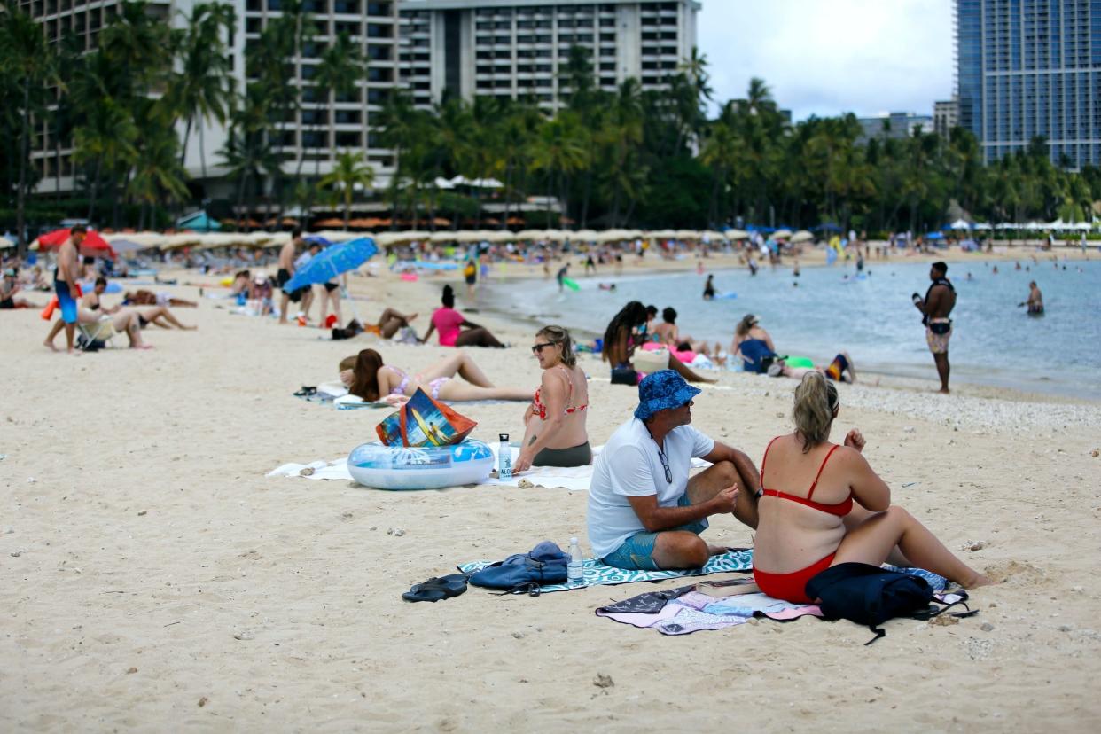 Brett Walsh and Emma Yates sit in the sun on Waikiki Beach in Honolulu on May 23, 2022.