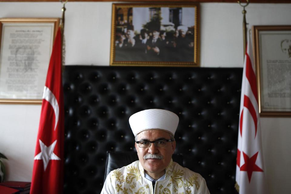 In this photo taken on Monday, April 14, 2014, Cyprus’ Grand Mufti Talip Atalay, the religious affairs leader of Turkish Cypriots in the breakaway north of the ethnically split country, is seen during an interview at his office in northern part of the divided capital Nicosia. In the background are the portraits of the Turkish Cypriot leader Dervis Eroglu, left, and former Turkish Cypriot leader Rauf Denktash, centre. For the first time in nearly 60 years, a Good Friday service was held at the 14th-century church of Agios Georgios Exorinos in the medieval center of Famagusta. Cyprus was divided along ethnic lines in 1974 into a Greek Cypriot south and Turkish Cypriot north after Turkey invaded following a coup aiming to unite the island with Greece. For decades, there was no contact between the religious leaders of the Christian Greek Cypriots and Muslim Turkish Cypriots. But that changed in 2009 with a kind of faith-based diplomacy that has quietly been conducted between the leader of the island’s Greek Orthodox Christian Church Archbishop Chrysostomos II and Turkish Cypriot Muslim Grand Mufti Talip Atalay. (AP Photo/Petros Kardjias)