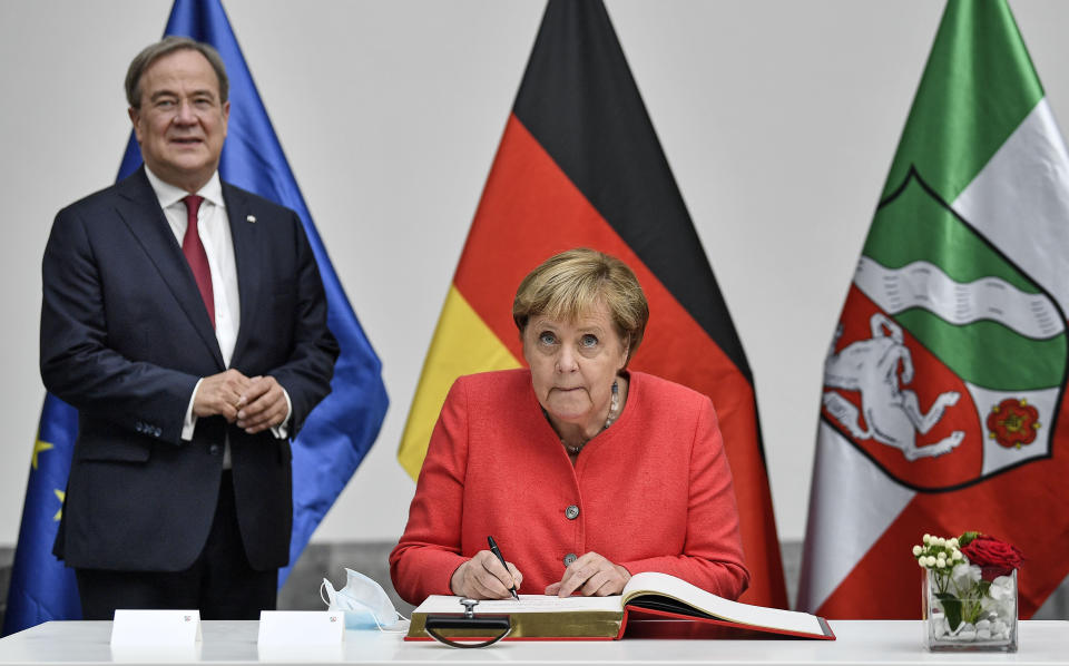 FILE - In this Aug. 18, 2020 file photo, German chancellor Angela Merkel, right, signs a golden book as she meets Governor Armin Laschet, left, during her visit at Germany's most populated province North Rhine-Westphalia in Duesseldorf, Germany. Like Merkel, Laschet is known as a centrist favoring integration over polarization. So far, he has been guarded in deviating from her successful middle-of-the-road path on domestic issues. (AP Photo/Martin Meissner, File)