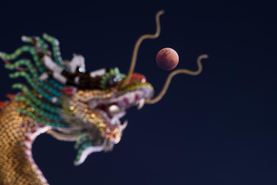 <p>The moon rises over the horizon above the head of a Chinese dragon statue at a Buddhist temple in Bangkok on Jan. 31, 2018. (Photo: Roberto Schmidt/AFP/Getty Images) </p>