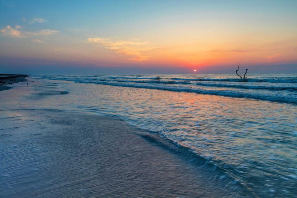 Rosy glow of the sun as it appears above the horizon of the Gulf of Mexico in Padre Island National Park, with pastel colors and an orange reflection of the sunlight in the water