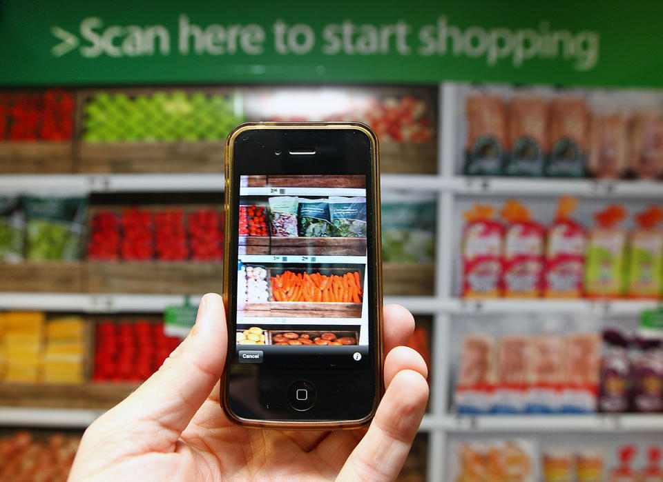 Hand holding a smartphone camera in front of grocery shelves, with sign that reads 