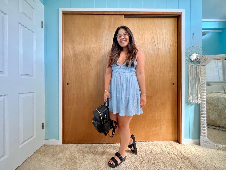 Author poses while wearing baby blue dress, black backpack, and black sandals.