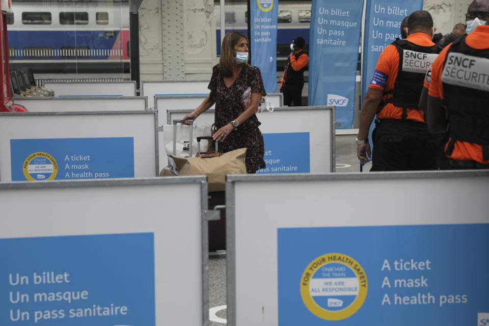 A woman walks past signs reading "A ticket, a mask, a health pass" at the Gare de Lyon train station in Paris Monday Aug.9, 2021. Starting today, the pass will be required in France to access cafes, restaurants, long-distance travel and, in some cases, hospitals. It was already in place for cultural and recreational venues, including cinemas, concert halls, sports arenas and theme parks with a capacity for more than 50 people. (AP Photo/Adrienne Surprenant)