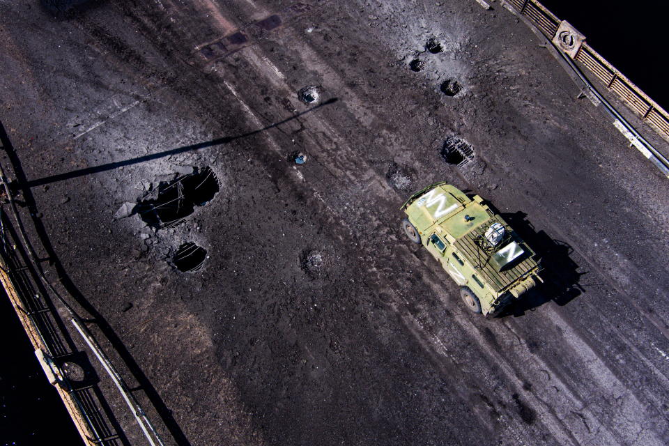 A huge crater in the asphalt in a road bridge is flanked by an armored personnel carrier marked Z.