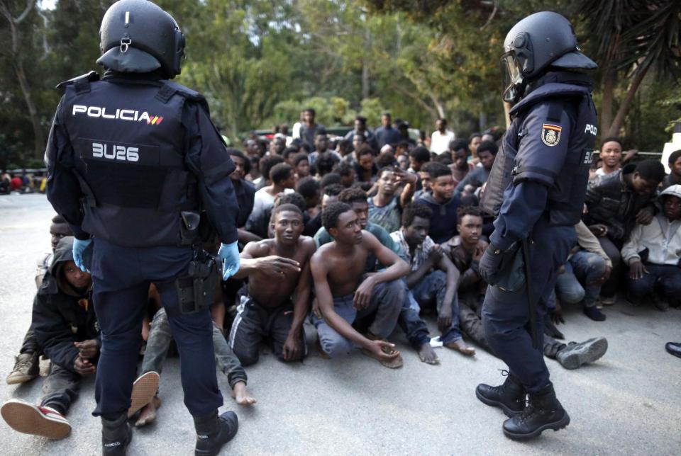 Migrants sit on the ground next to Spanish police officers after storming a fence to enter the Spanish enclave of Ceuta, Spain, Friday, Feb. 17, 2017. An emergency team in Ceuta is assisting more than 300 migrants who crossed the fence surrounding Spain's enclave in North Africa early Friday, a spokesman for the local Red Cross said. (AP Photo/Jesus Moron)