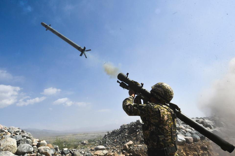 A solider fires a portable air-defense system beside a stone wall under a blue sky