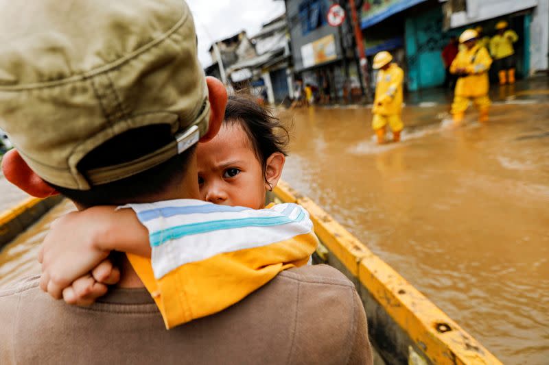 A girl is carried by her father across floodwaters in the Jatinegara area after heavy rains in Jakarta