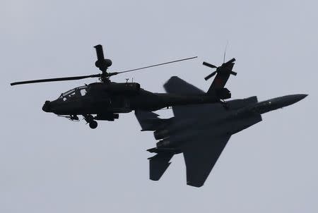 A Republic of Singapore Air Force (RSAF) F-15SG fighter aircraft performs a maneuver as it flies past an RSAF AH-64D Apache helicopter during a preview of the Singapore Airshow at Changi exhibition center in Singapore February 14, 2016. REUTERS/Edgar Su