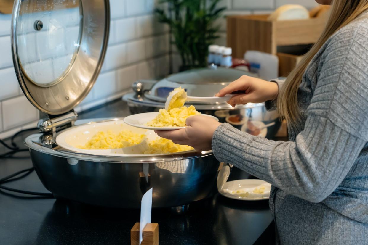 No face woman putting scrambled eggs in a self-service buffet with hot breakfast in the hotel. Continental breakfast concept. Selective focus, copy space