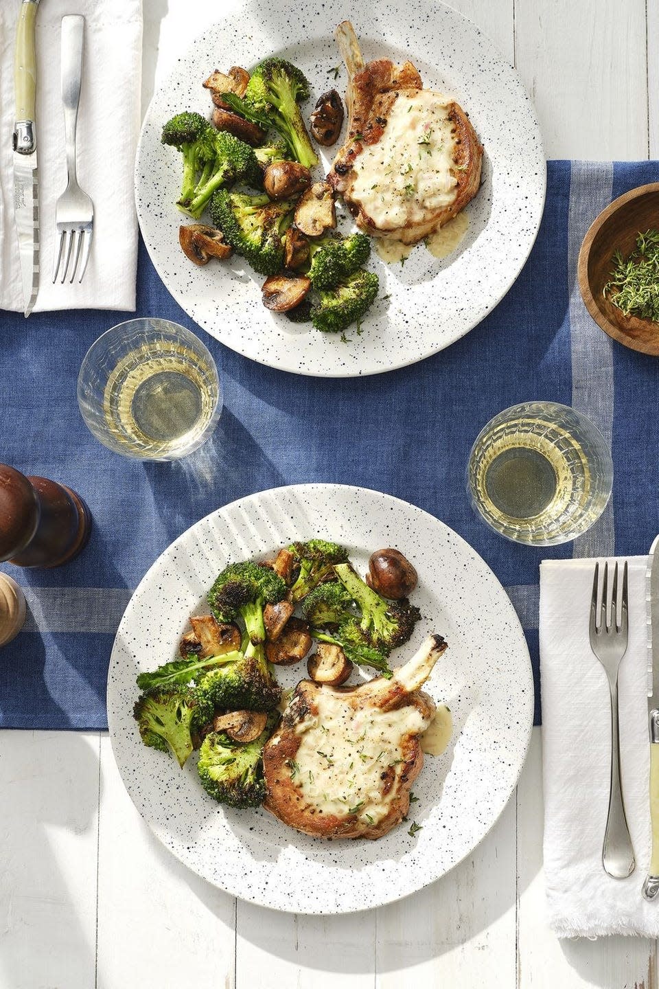 smothered pork chops with broccoli and mushrooms on a white speckled plate with a fork