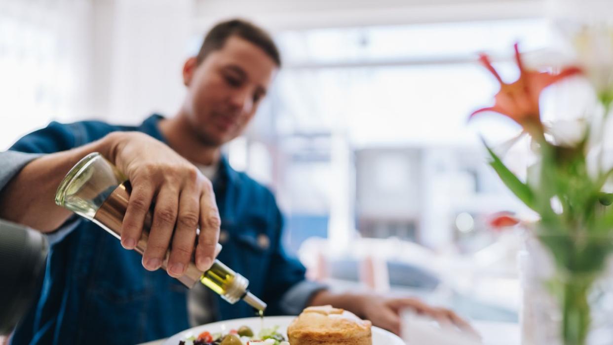 close up of man pouring olive oil on salad at restaurant