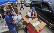 Wearing masks amid concerns of the spread of COVID-19, volunteers Karen Cooperstein, right, and Edwin Chinchilla, left, prepare food for the pubic during a drive through food pantry distribution by Catholic Charities in Dallas, Thursday, July 2, 2020. (AP Photo/LM Otero)